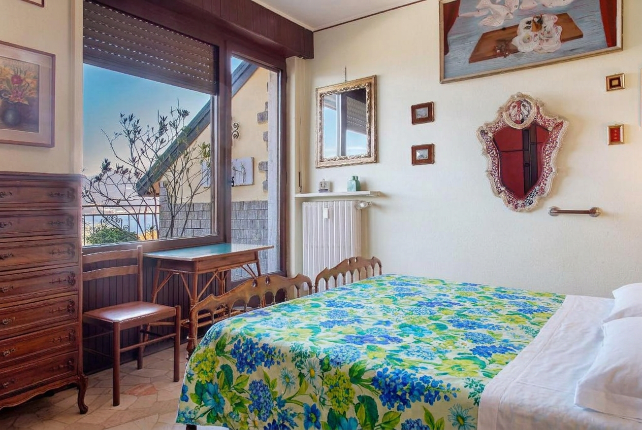 Camera da letto matrimoniale con copriletto estivo fiorito blu e verde e vista lago